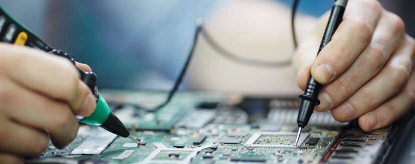 Closeup shot of male hands testing electric current voltage in circuit board of disassembled laptop using multimeter tool on table in maintenance shop
